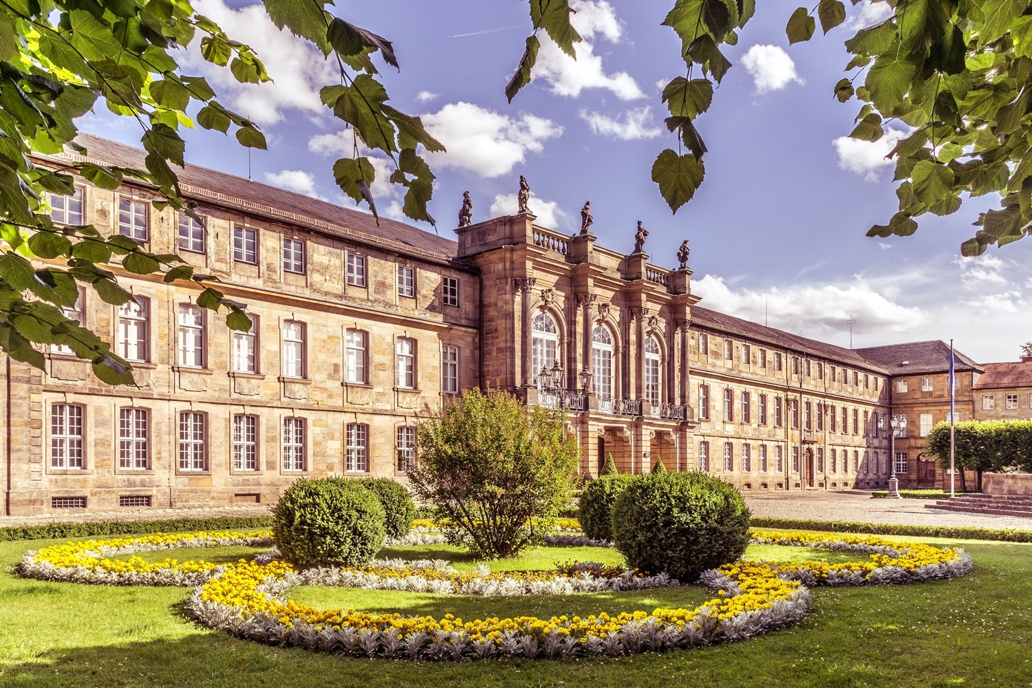 Das Neue Schloss in Bayreuth. Im Vordergrund sieht man blühende Blumen und Sträucher