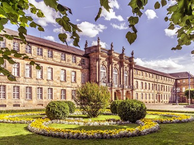 Das Neue Schloss in Bayreuth. Im Vordergrund sieht man blühende Blumen und Sträucher