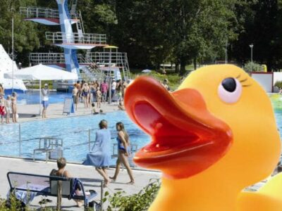 Quietscheente im Vordergrund, dahinter Freibadtreiben