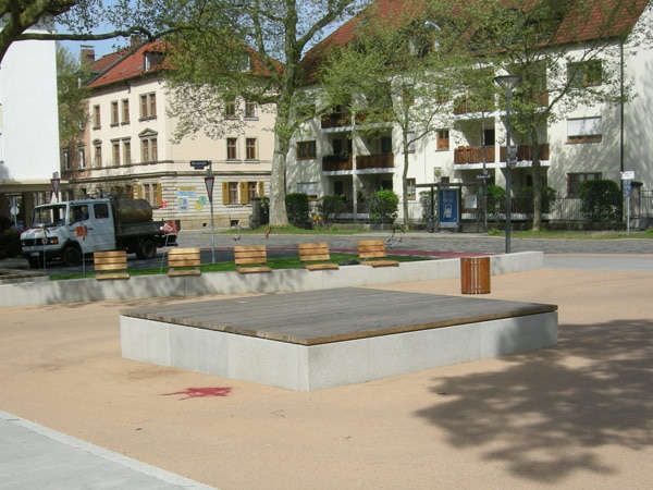 Foto Sitzinsel aus rechteckigem Betonblock mit Holzabdeckung und Sitzblöcken aus Holz auf Betonmauer