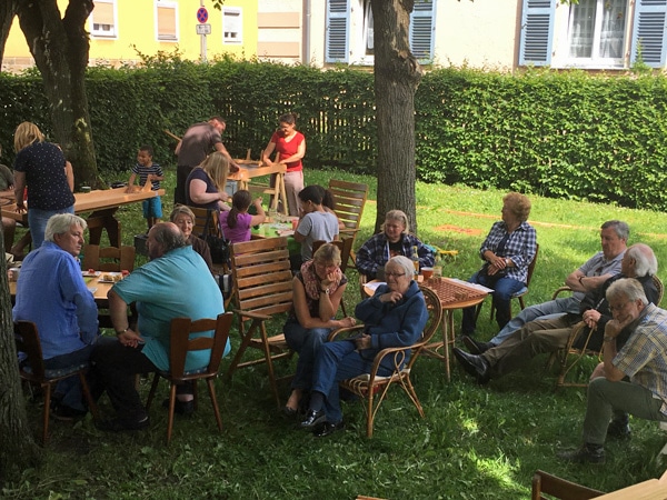 Personen sitzen an Tischen im Schatten der Bäume im Garten des Hammerstätter Hofs