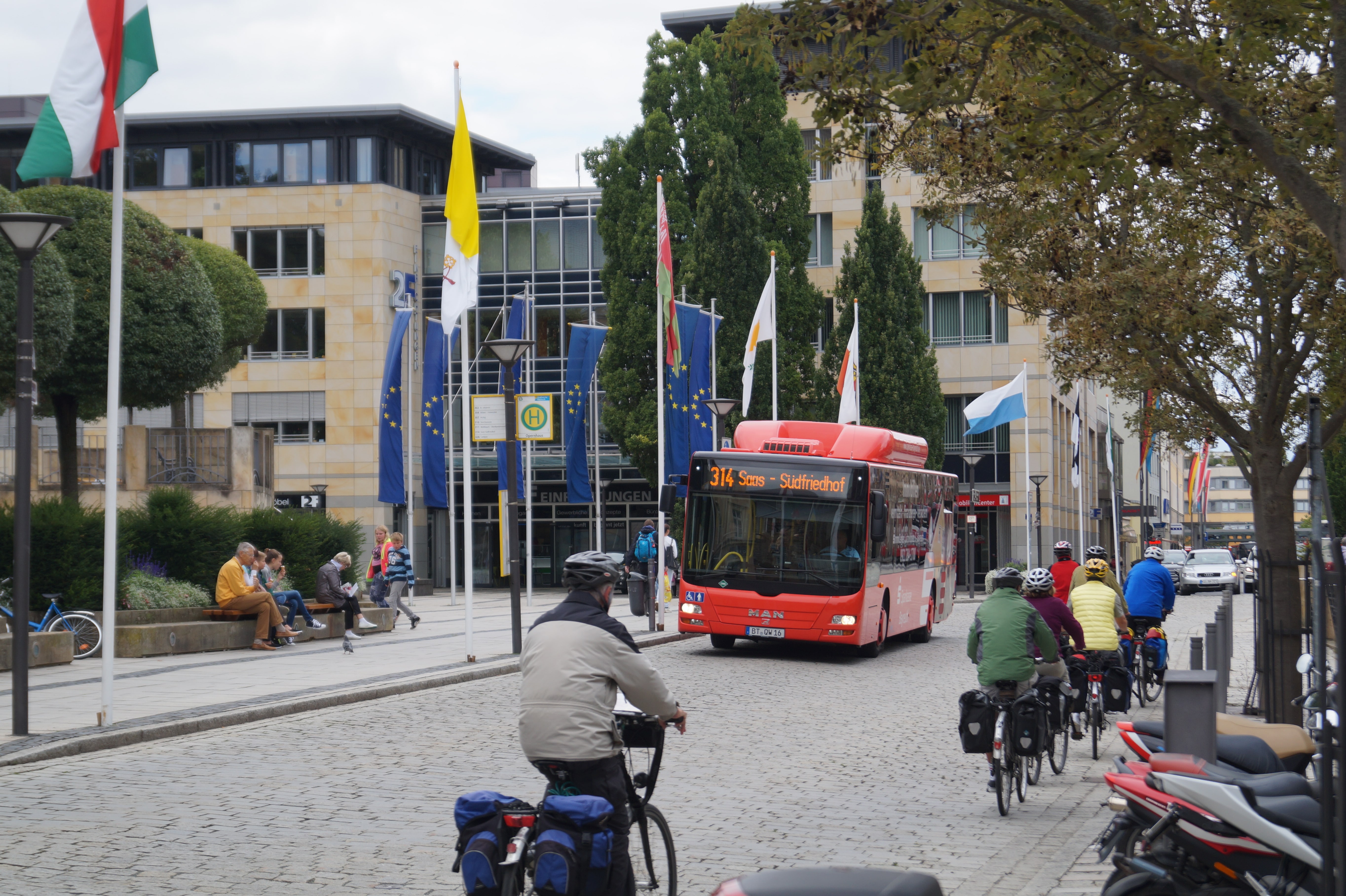 fahrende Radfahrer und entgegenkommender Stadtbus, sowie Passanten auf dem Bürgersteig