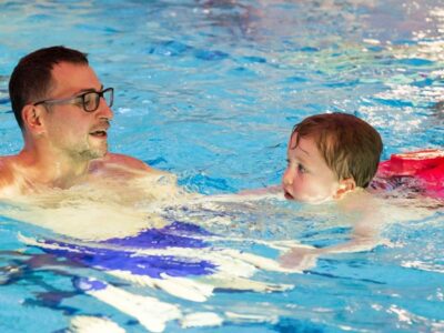 Ein Mann schwimmt mit einem kleinen Kind im Wasser.