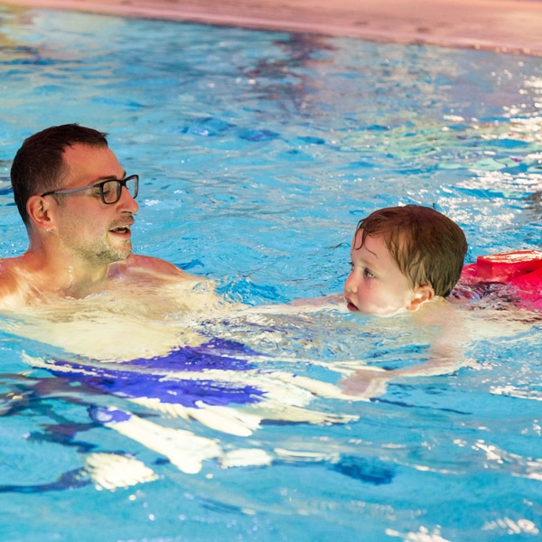 Ein Mann schwimmt mit einem kleinen Kind im Wasser.