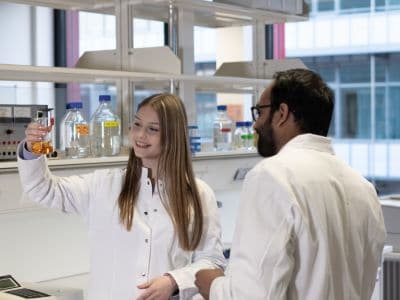 Junge Frau betrachtet ein Reagenzglas im Labor der Universität Bayreuth