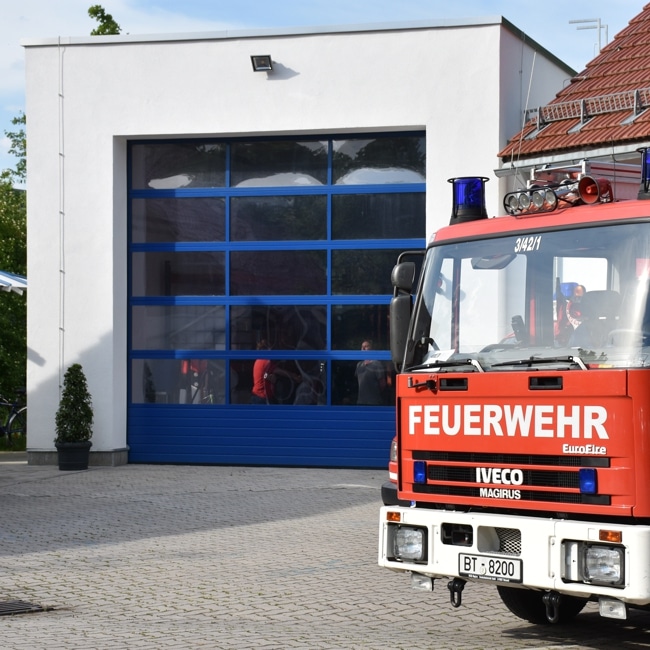 Ein Feuerwehrauto steht vor einem blauen Rolltor.