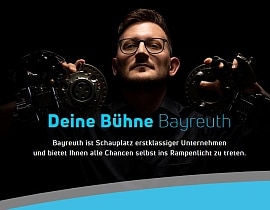 Ein junger Mann hält zwei Eisen-Formteile hoch. Darunter steht: Deine Bühne Bayreuth