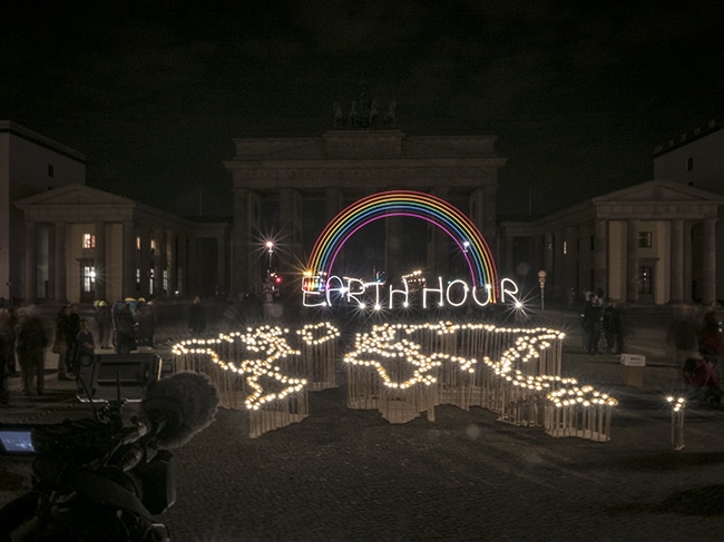 Die Umrisse der Weltkarte sind mit kleinen Lampen nachgezeichnet, darüber prangt ein Lichter-Regenbogen mit dem Schriftzug Earth Hour.