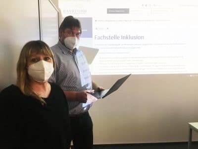 Frau Lebershausen (Fachstelle Inklusion) und Herr Höhmann (Mitglied des Behindertenbeirates) stehend vor Leinwand mit Bild der Homepage der Fachstelle Inklusion im Hintergrund.