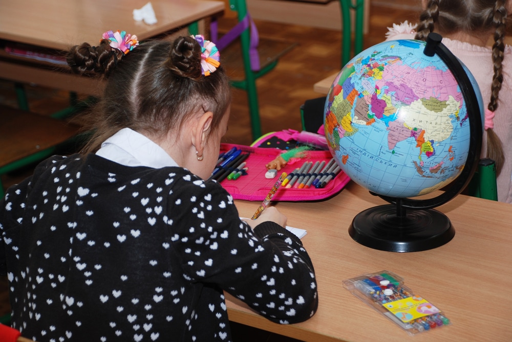 Mädchen sitzt am Schultisch mit Globus