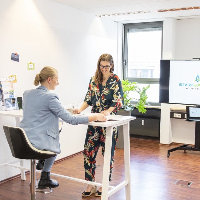Büroraum mit zwei jungen Frauen an einem Besprechungstisch.