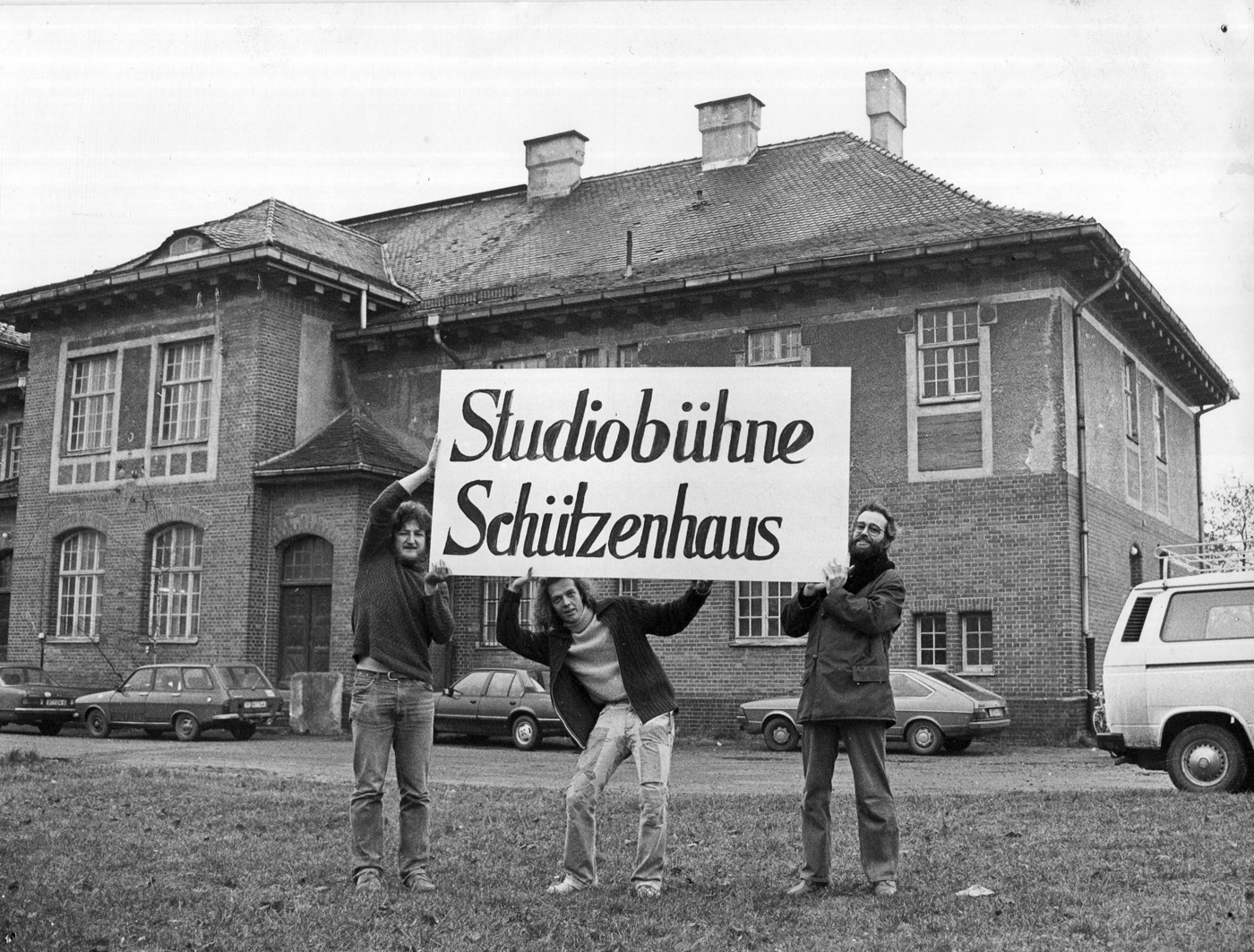 DRei junge Männer halten ein Schild hoch, auf dem "Studiobühne Schützenhaus" steht.