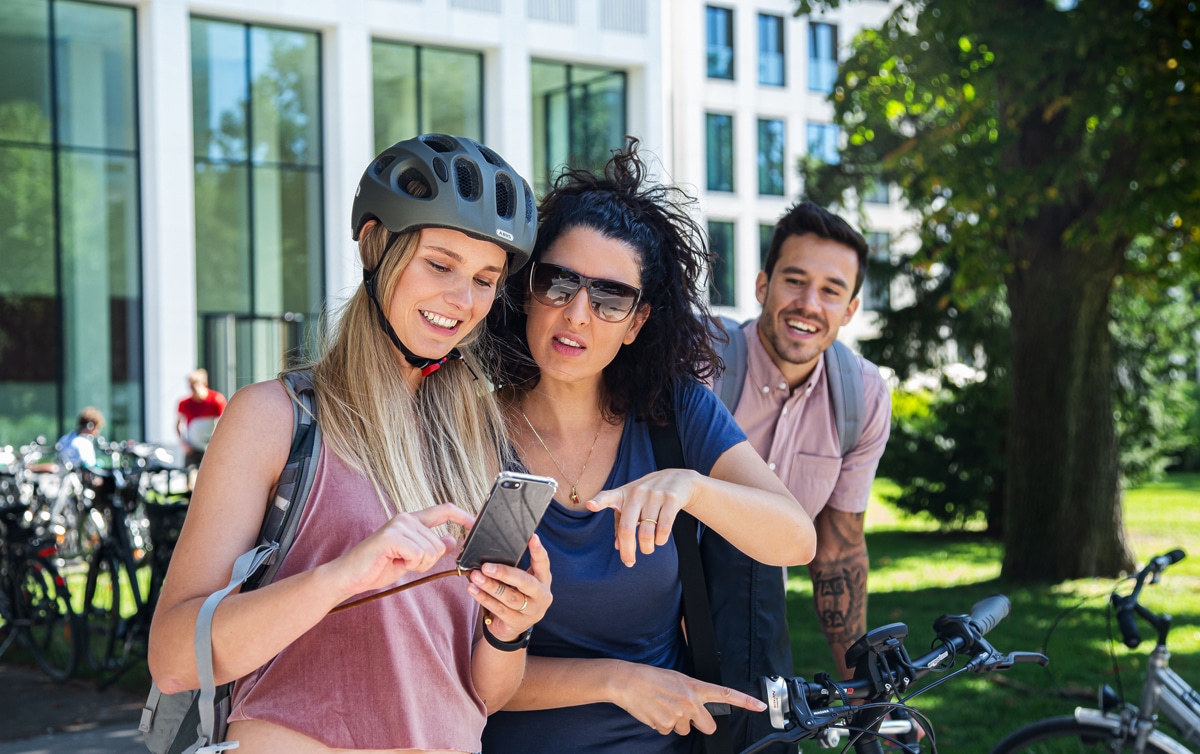 Zwei junge Frauen mit Fahrrad schauen aufs Handy. Foto: Laura Nickel