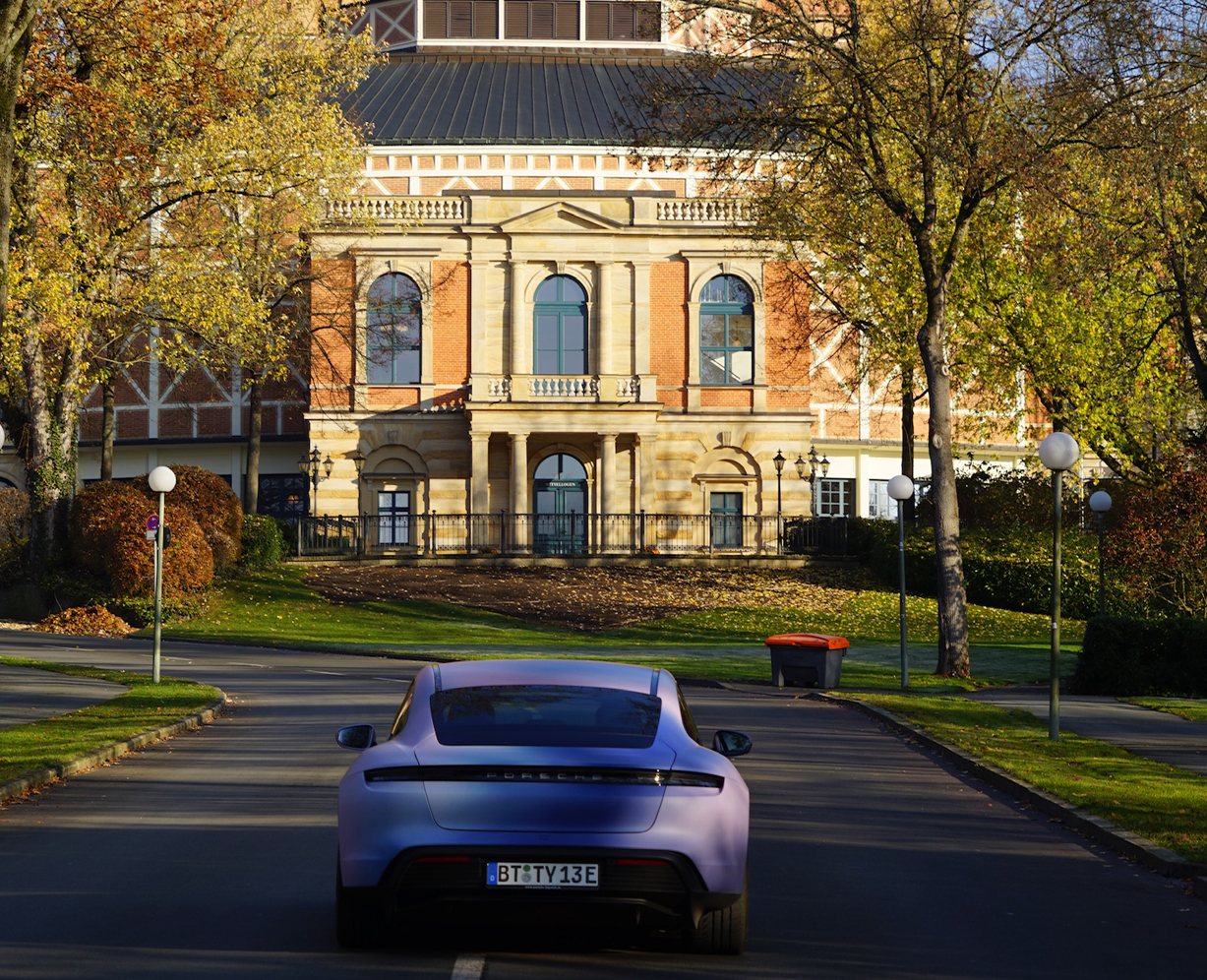 Ein Auto fährt auf das Bayreuther Festspielhaus zu.