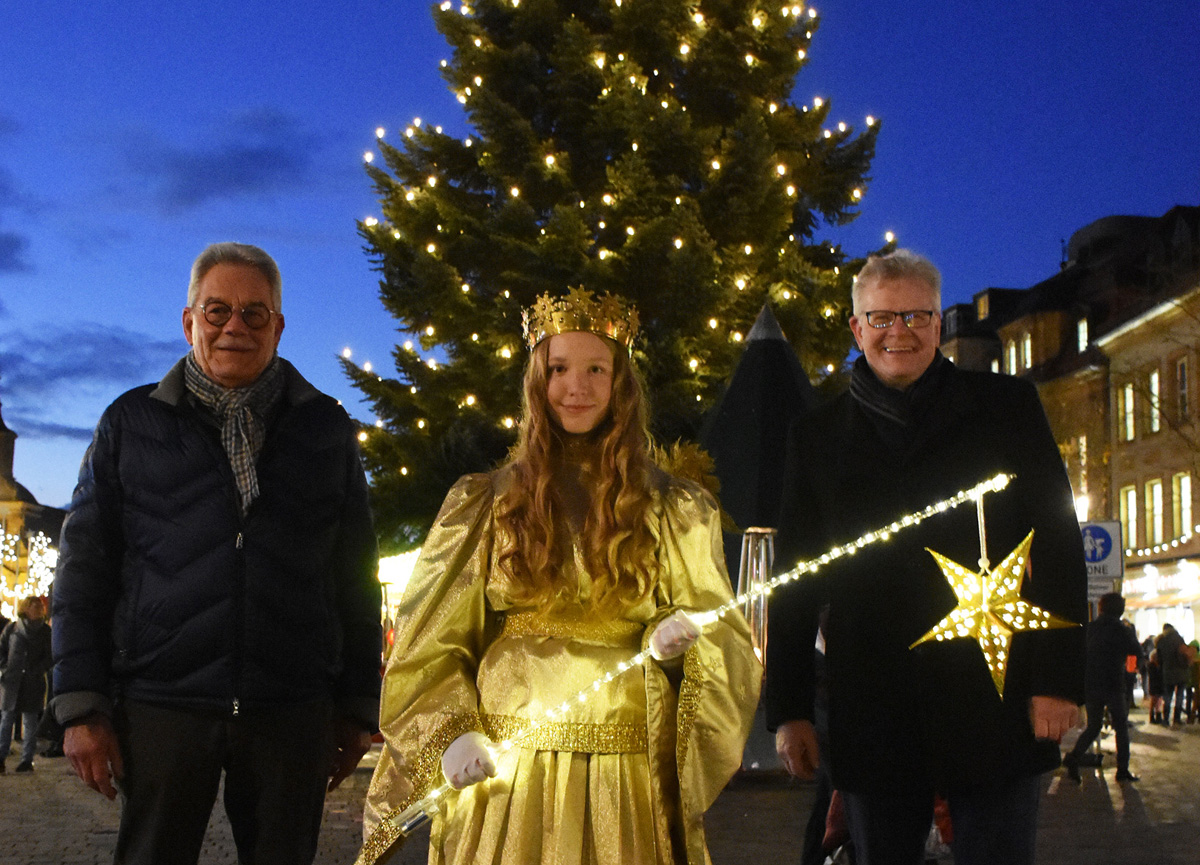 Das Bayreuther Christkind Amelie Ludwig steht im goldenen Kleid gemeinsam mit OB Ebersberger und Diebert Loher vor einem beleuchteten Weihnachtsbaum.