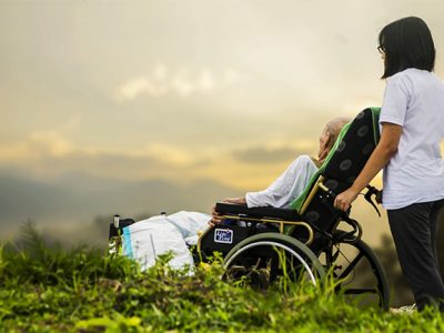 Frau schiebt pflegebedürftige Person im Rollstuhl