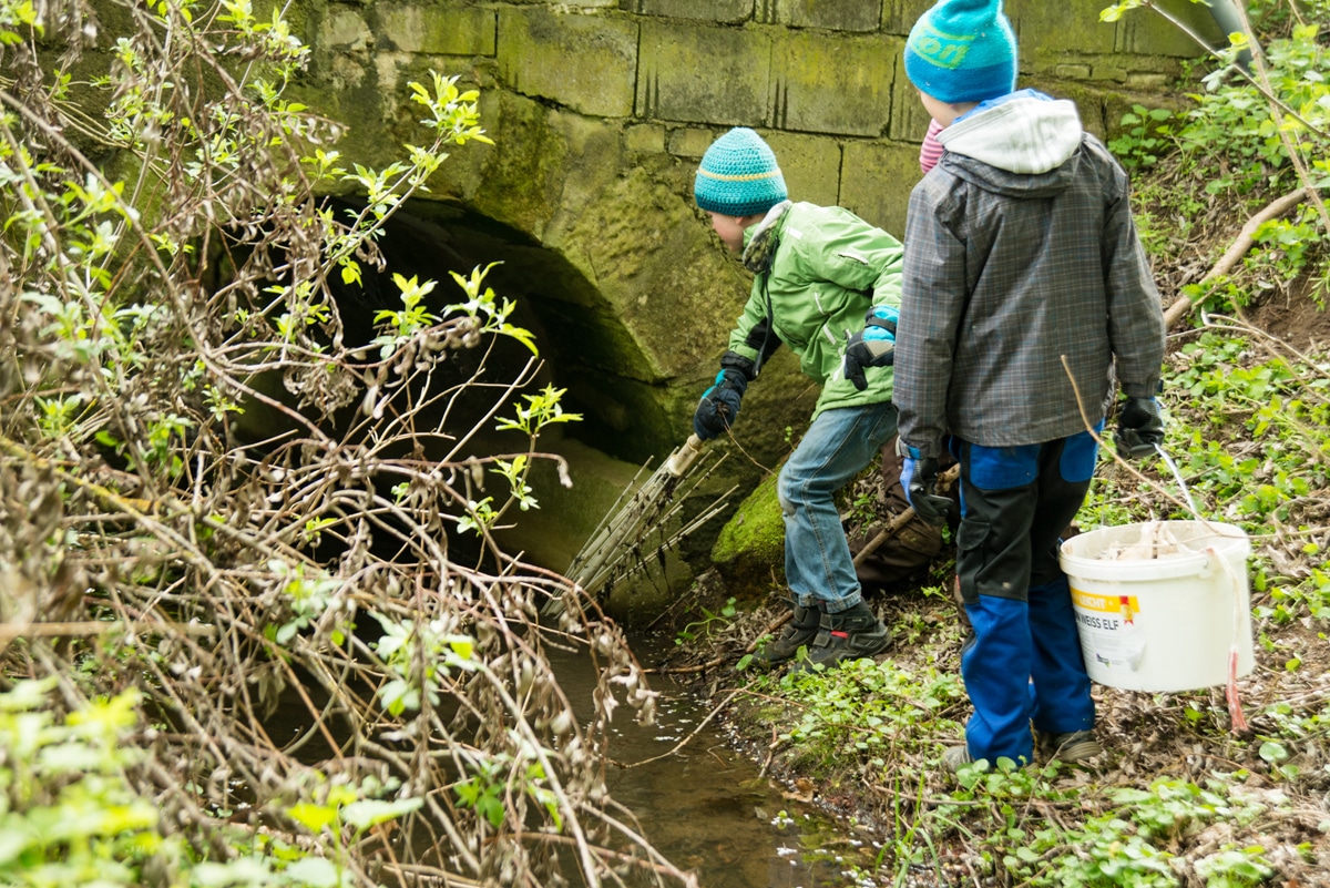 Zwei Buben säubern einen Flusslauf an einer Brücke.