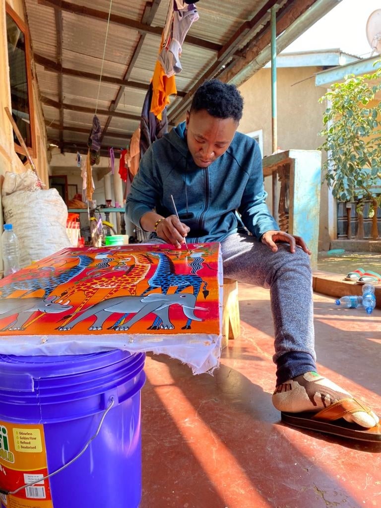 Der tansanische Künstler Allen Enock Abeid malt am Boden mit bunten Farben auf einen Leinwand.