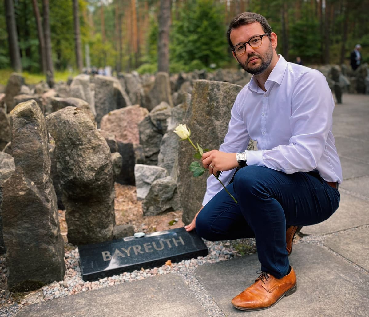 Bürgermeister Zippel mit Rose in der Hand berührt den Gedenkstein mit dem Logo der Stadt Bayreuth