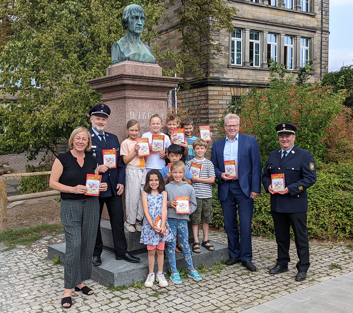 FFW-Hausaufgabenhefte-Ubergabe-9 Menschen- und Kindergruppe vor dem Denkmal von J. Graser an der Graserschule