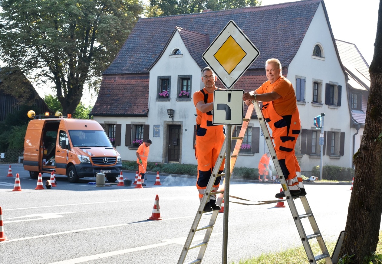 Zwei Bauhofmitarbeiter auf Leitern an einem Vorfahrtsschild.