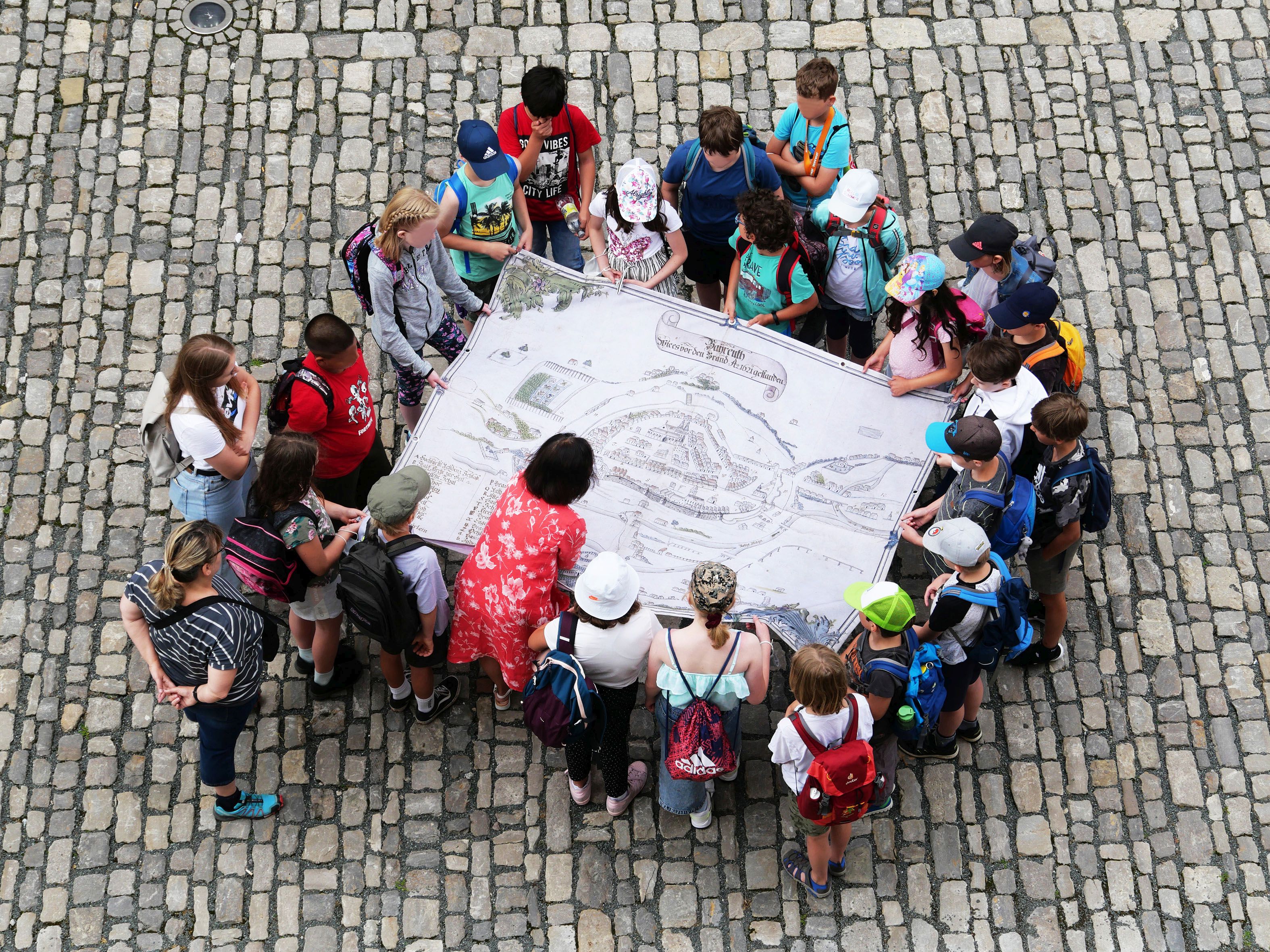 Blick von oben auf eine Gruppe Kinder, die sich im Rahmen einer museumspädagogischen Führung mit einem alten Stadtplan Bayreuths beschäftigen