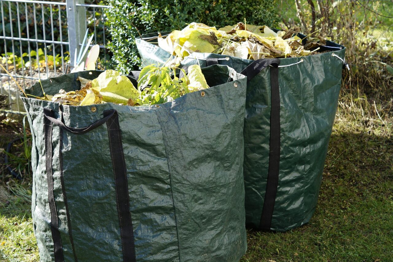 Zwei grüne Sammelsäcke voller Gartenabfälle.