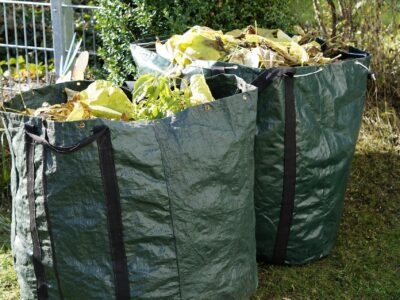 Zwei grüne Sammelsäcke voller Gartenabfälle.