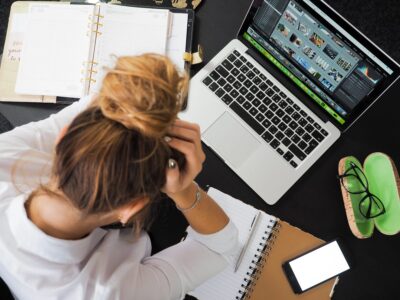 Eine junge Frau sitz mit über dem Kopf geschlagenen Händen vor einem Laptop