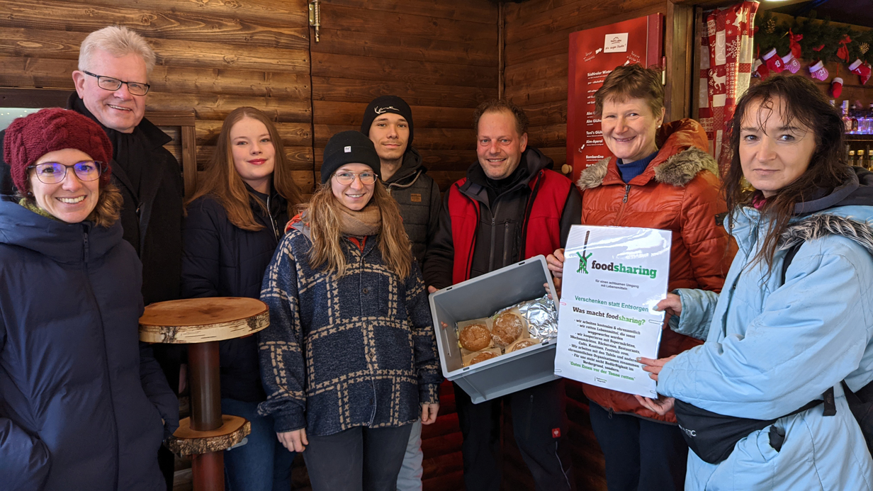 OB Ebersberger, Vertreterinnen der Stadtverwaltung und der Initiative Foodsharing stehen in einer Bude des Christkindlesmarktes.