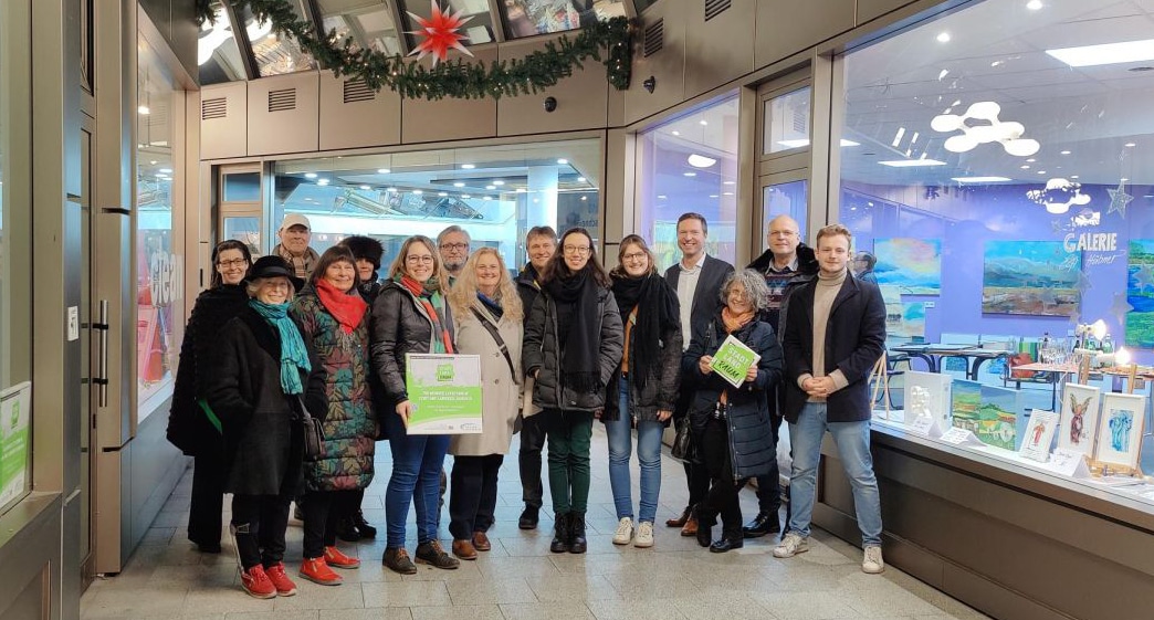 Eine Gruppe von Frauen und Männern steht vor einem Schaufenster in einer Fußgängerpassage.