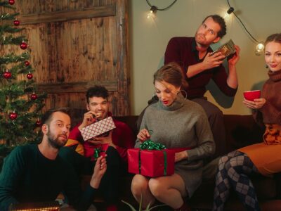 Fünf Männer und Frauen sitzen vor einem Weihnachtsbaum und betrachten Präsente. | Foto: Quintense