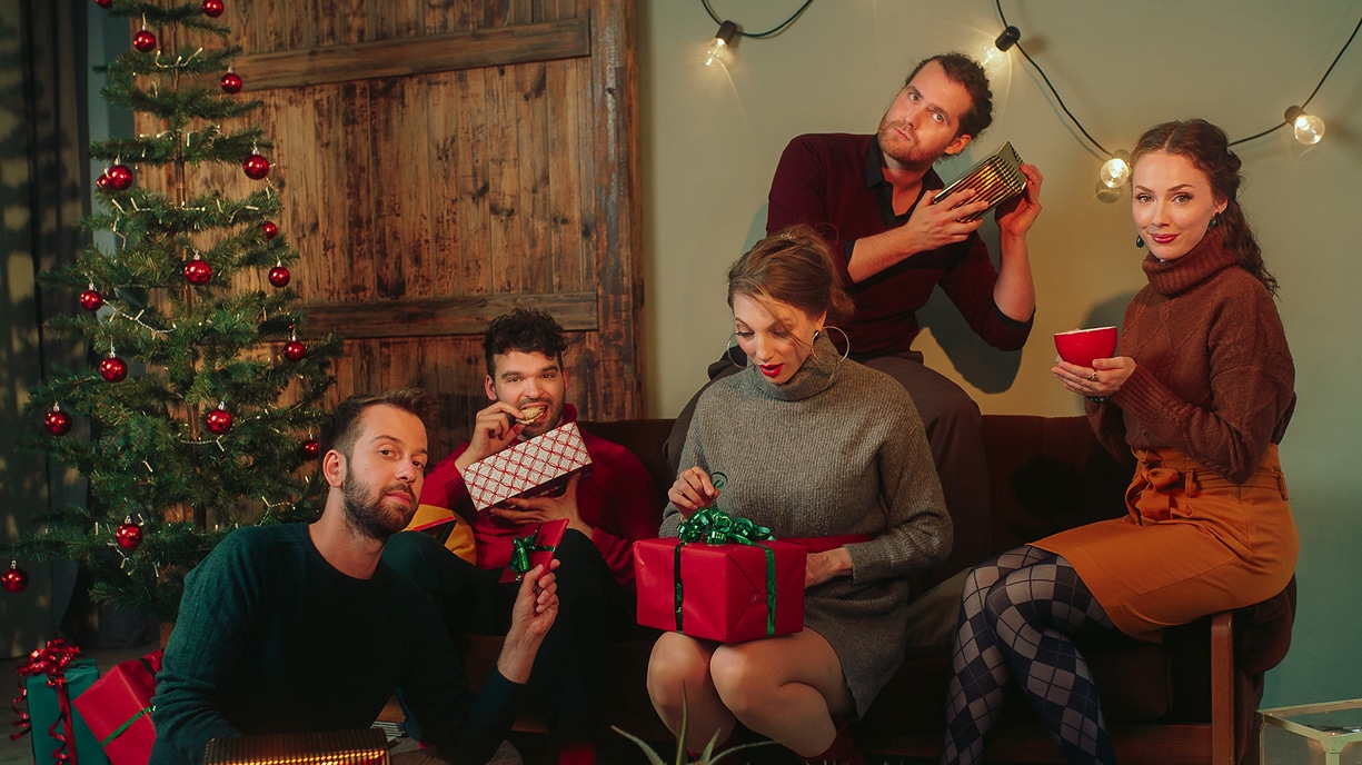 Fünf Männer und Frauen sitzen vor einem Weihnachtsbaum und betrachten Präsente. | Foto: Quintense