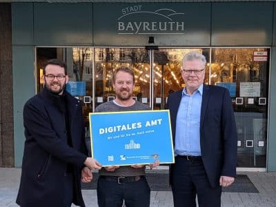 Bürgermeister Zippe, Mitarbeiter Kollenda und Oberbürgermeister Ebersberger präsentieren die Plakette "Digitales Amt" vor dem Eingang des Rathauses.