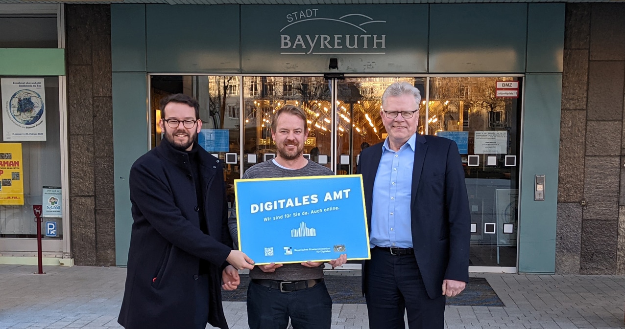 Oberbürgermeister Thomas Ebersberger, 2. Bürgermeister Andreas Zippel und der städtische Digitalisierungsbeauftragte Matthias Kollenda präsentieren die Plakette "Digitales Amt" vor dem Eingang zum Rathaus.