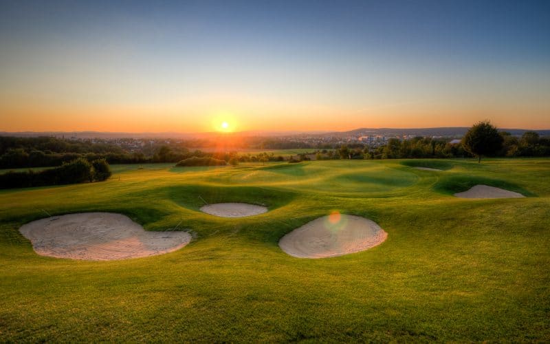 Golfplatz mit Sandbunker im Vordergrund und untergehender Sonne im Hintergrund.