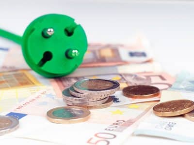 Ein grüner Elektrostecker liegt auf Geldscheinen, drumherum liegen Münzen.