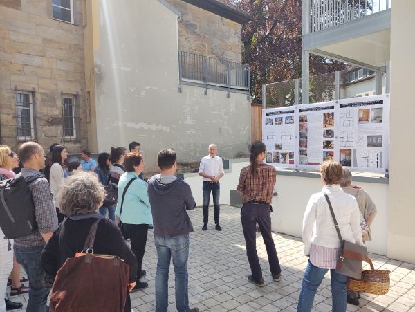 Besuchergruppe im Hinterhof, Architekt erläutert anhand Plänen