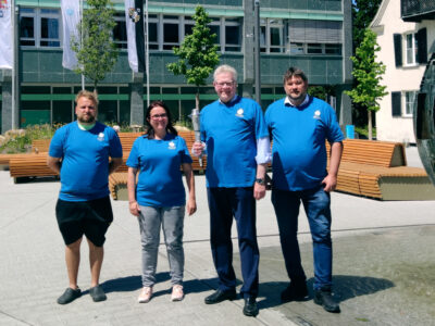 Drei Männer und eine Frau in blauen T-Shirts präsentieren die Fackel für die Special Olympics World Games vor dem Rathaus.