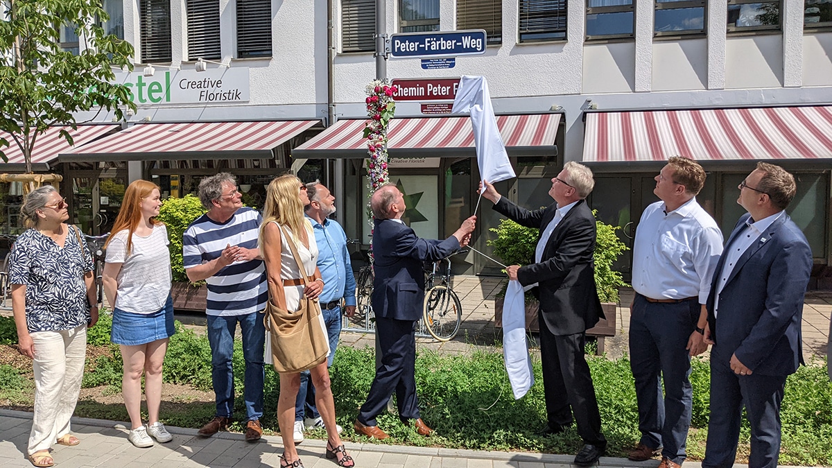 Mehrere Personen stehen vor einem Straßenschild, das soeben enthüllt wurde.