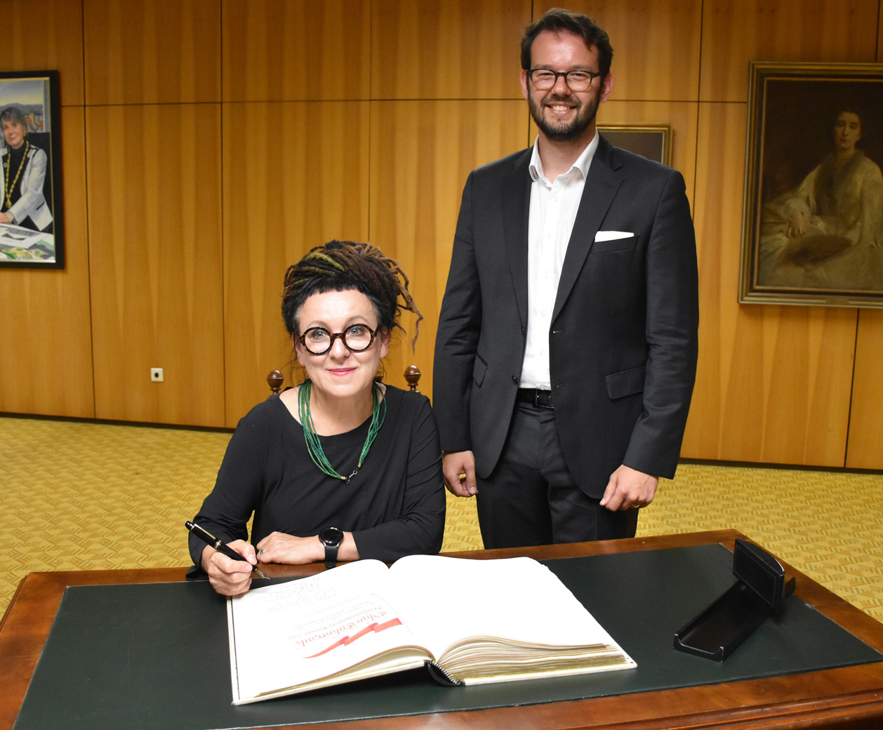 goldenes buch 01 Olga Tokarczuk sitzt an einem Schreibtisch und trägt sich in ein Buch ein.