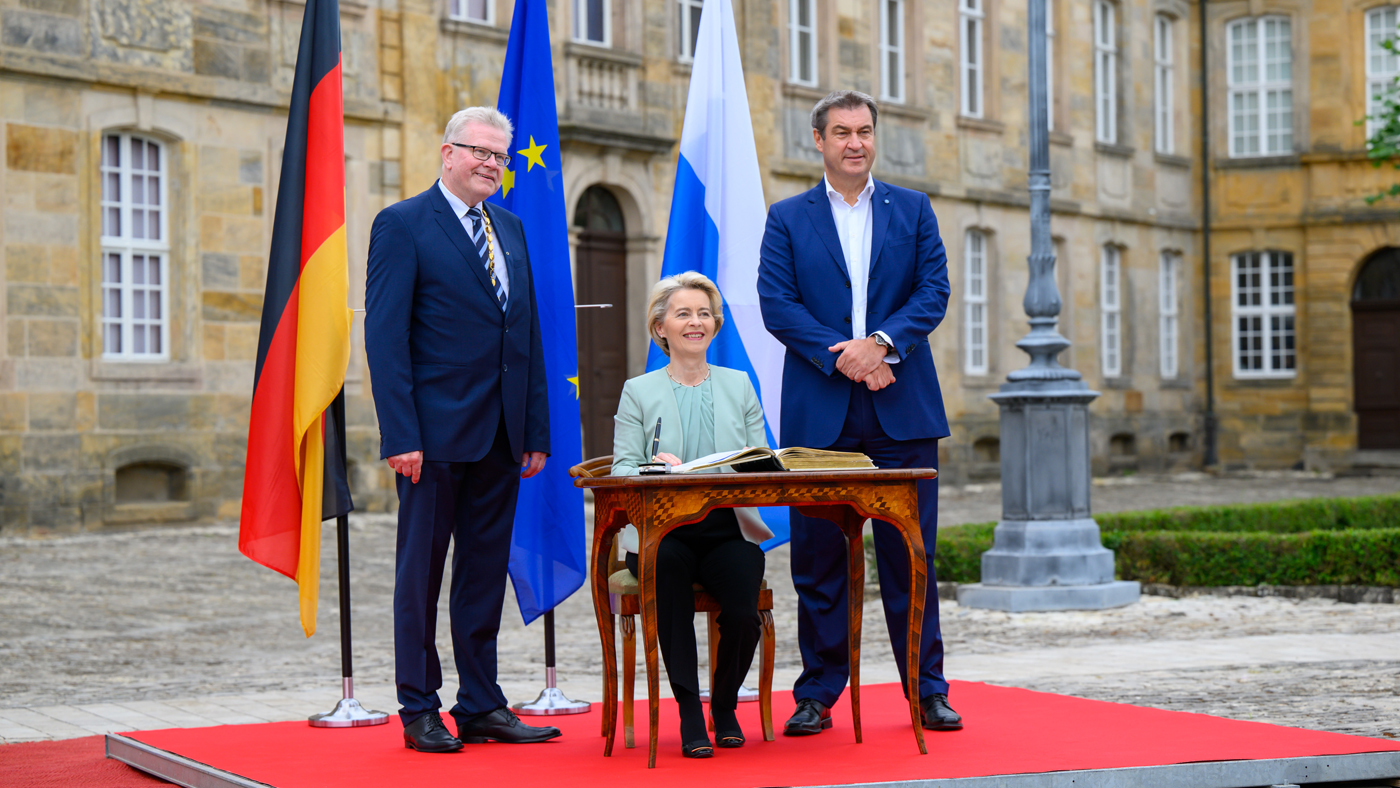 Bayerns Ministerpraesident Dr. Markus Soeder: Kabinettssitzung Bayreuth mit EU-Kommissionspräsidentin Ursula von der Leyen EU-Kommissionspräsidentin von der Leyen trägt sich in ein Buch ein. Neben ihr stehen Ministerpräsident Söder und Oberbürgermeister Ebersberger. | Foto: Bayerische Staatskanzlei