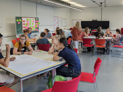 Junge Menschen sitzen an mehreren Tischen und diskutieren.