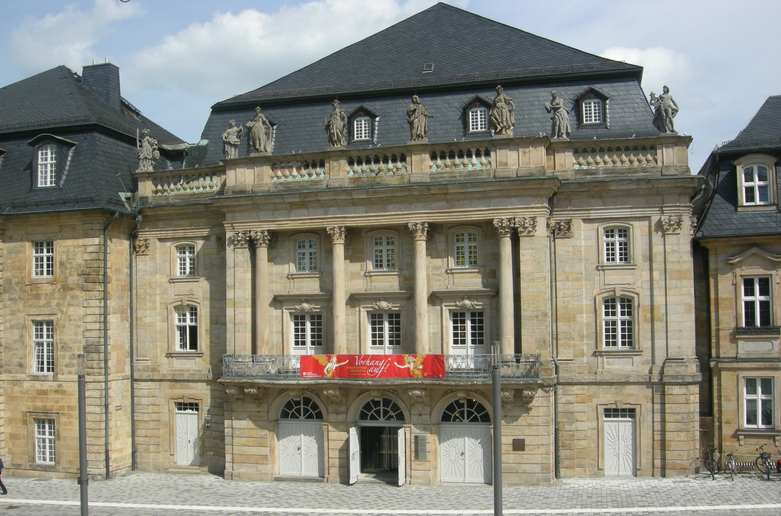 Eingangsansicht Markgräflichen Opernhaus - Sandsteinfassade mit Balkon, barocken Säulen und Skulpturen auf der Balustrade.