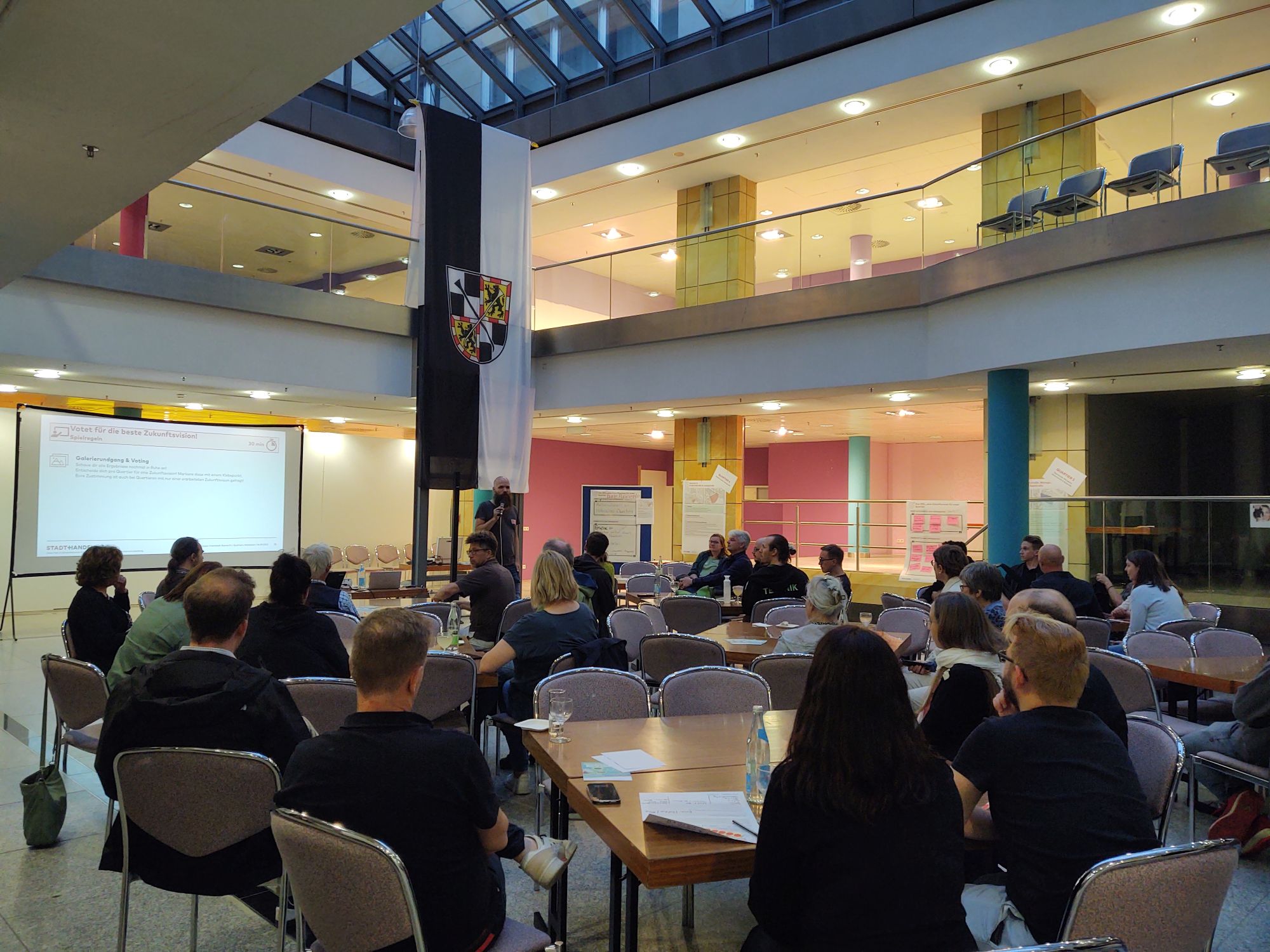 Menschen sitzen an Tischen im Atrium der Schlossgalerie - Moderator stellt Ergebnisse vor