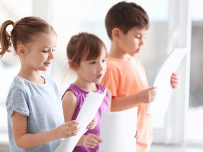 Drei singende Kinder mit Notenblättern in der Hand
