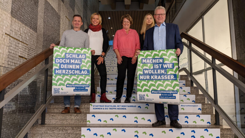 Ob Ebersberger und weitere Mitarbeiter stehen auf einer Treppe und halten Plakate in die Höhe.