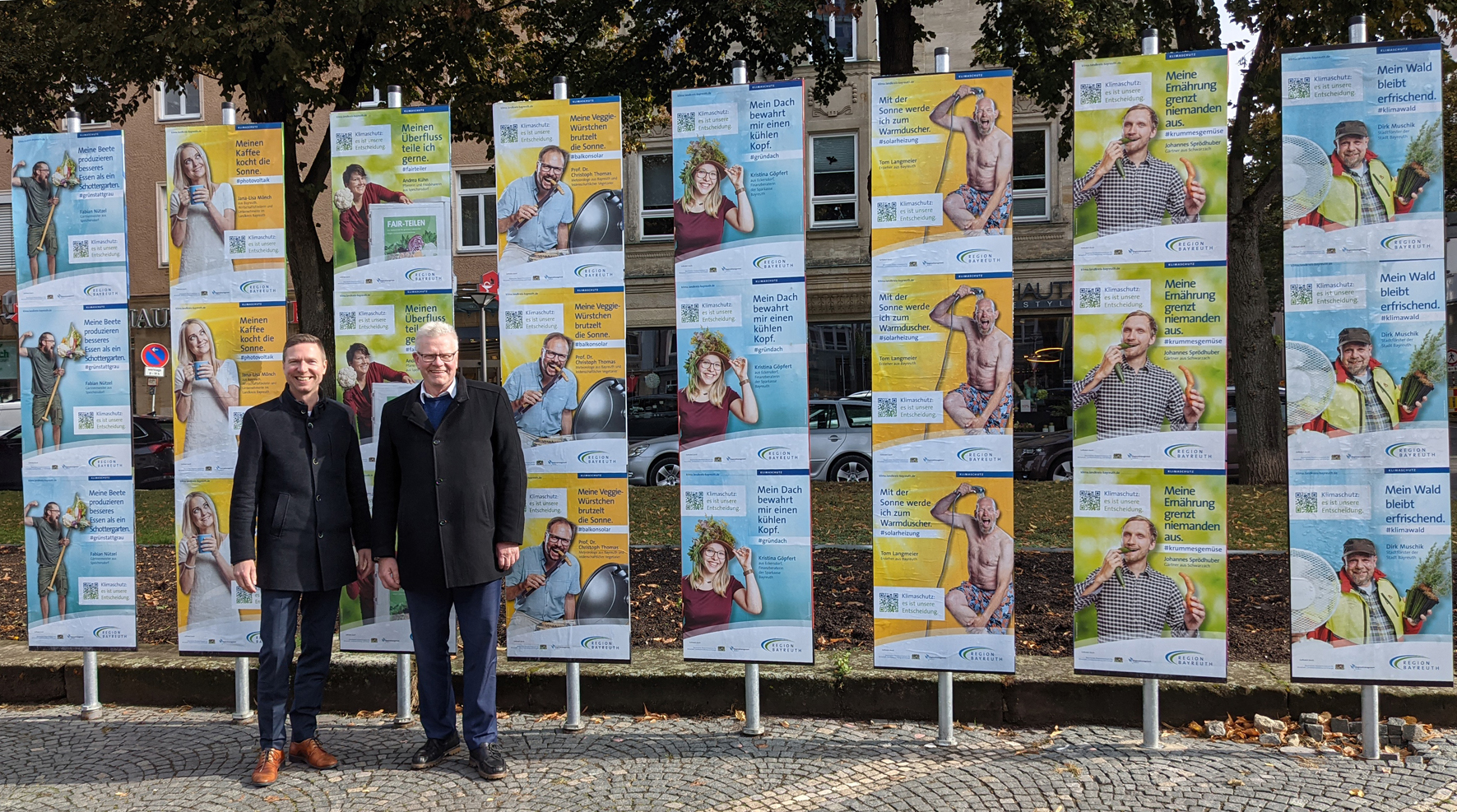 Landrat Wiedemann und Oberbürgermeister Ebersberger vor einer Plakatwand.