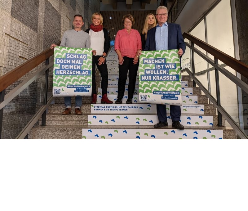 Ob Ebersberger und weitere Mitarbeiter stehen auf einer Treppe und halten Plakate in die Höhe.