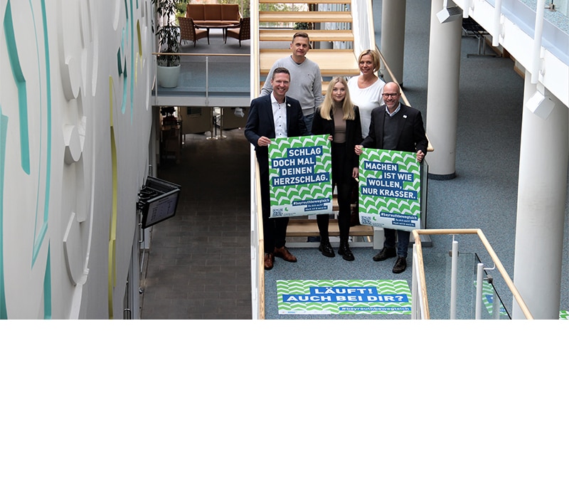 Fünf Mitarbeiter stehen auf einer Treppe und halten Plakate in die Höhe.